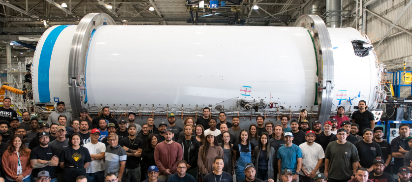 Parte da Equipe da SpaceX em frente a um estágio superior do Falcon 9 - Créditos: SpaceX